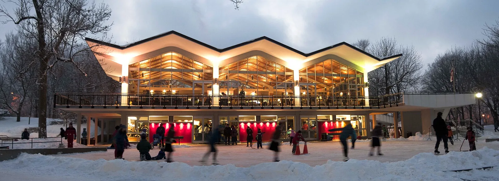 The Beaver Lake Pavilion lit up on a winter evening with skaters in front of it