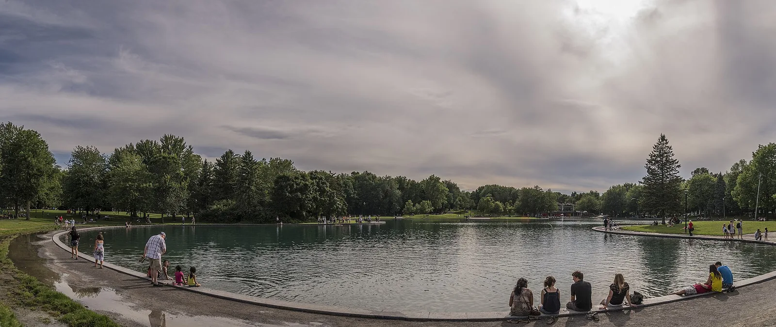 People sitting on the stone edge of Beaver Lake on a cloudy summer day, with trees along the far shore