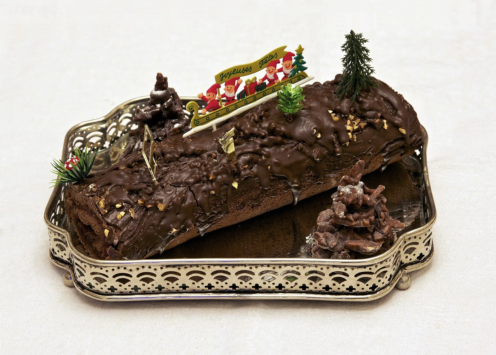 A chocolate bûche de Noël Yule-log cake decorated with small trees on a silver tray