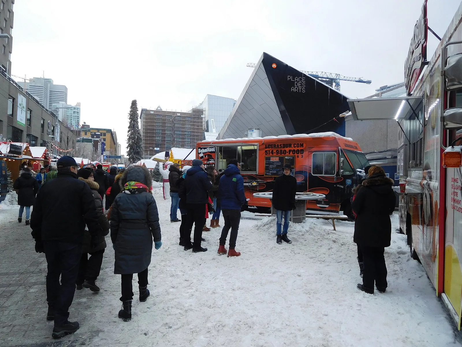 Shoppers walking between wooden chalets at a downtown Montreal Christmas market in the snow