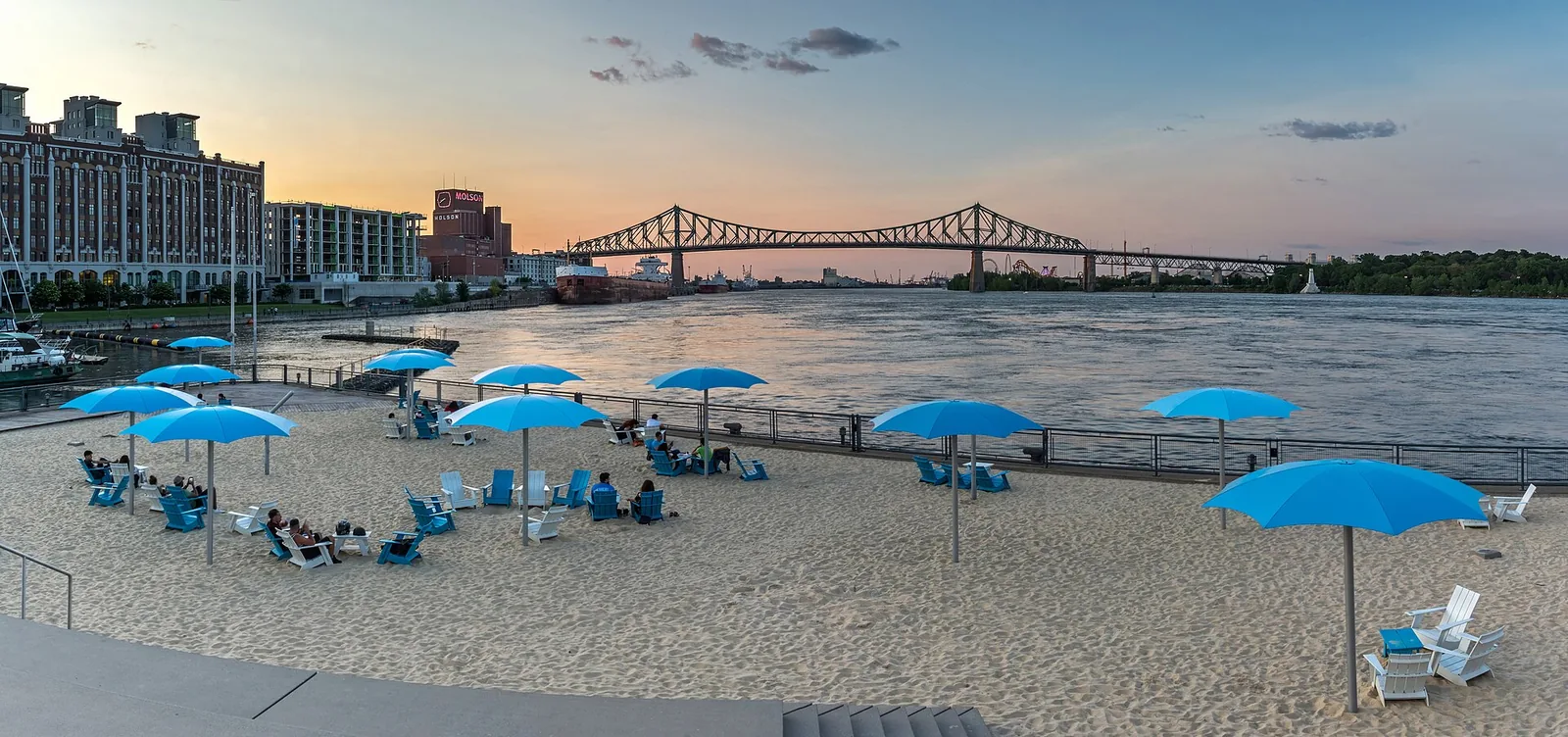 Blue parasols on the Clock Tower Beach at the Old Port at sunset, with the Jacques Cartier Bridge behind