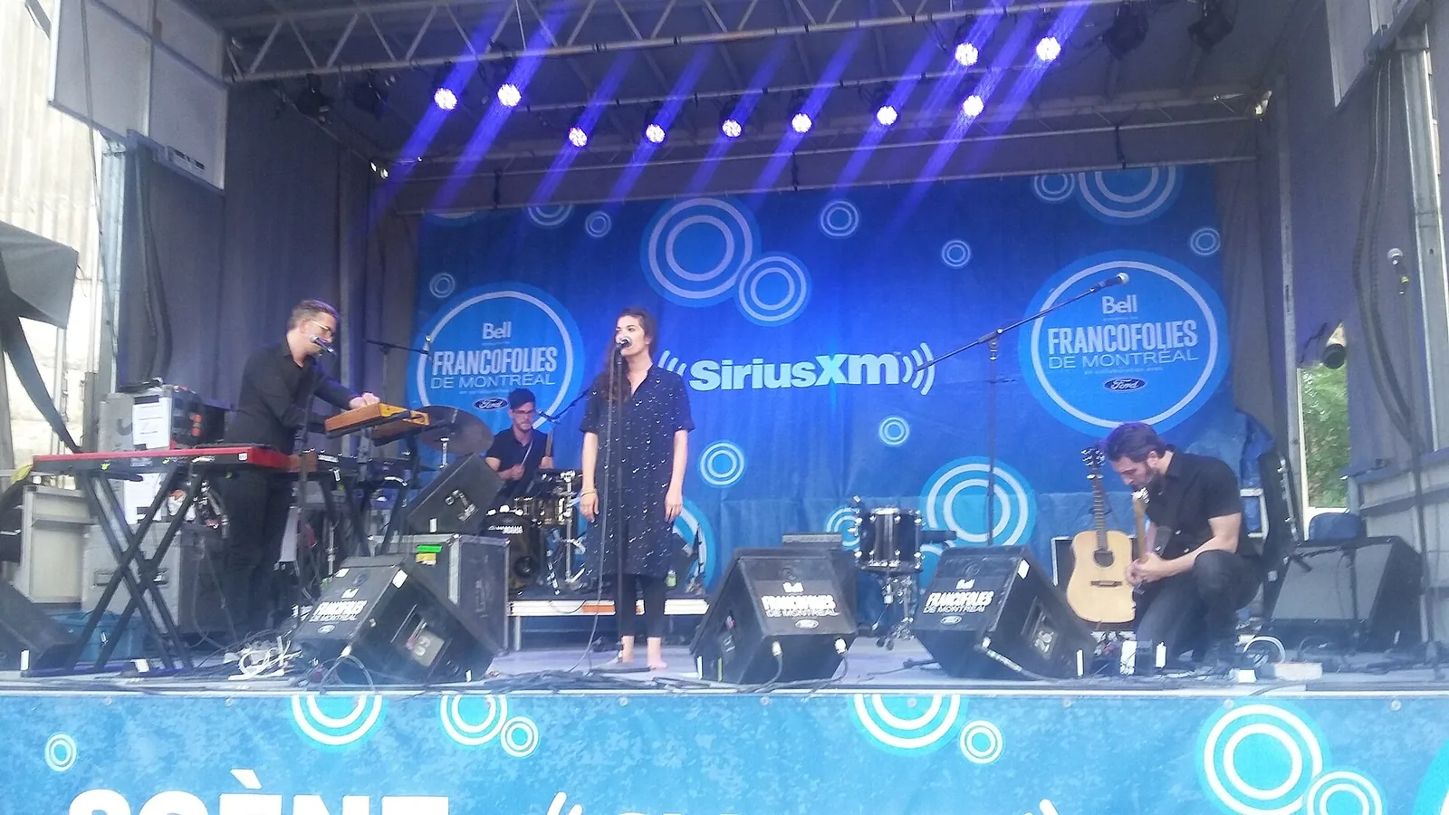 Band performing on a blue-lit outdoor stage at the Francofolies de Montréal, now the Francos