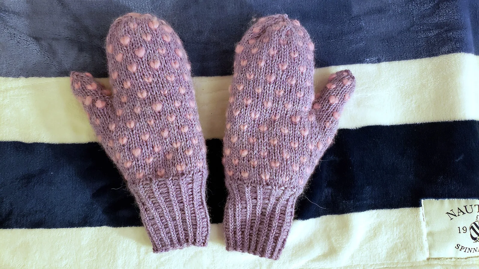 A pair of knitted wool mittens laid on a striped blanket