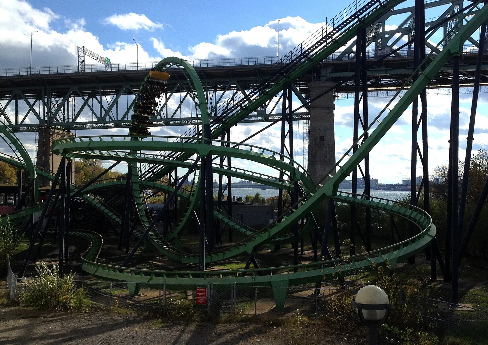 The green track of a roller coaster at La Ronde amusement park with the Jacques-Cartier Bridge behind