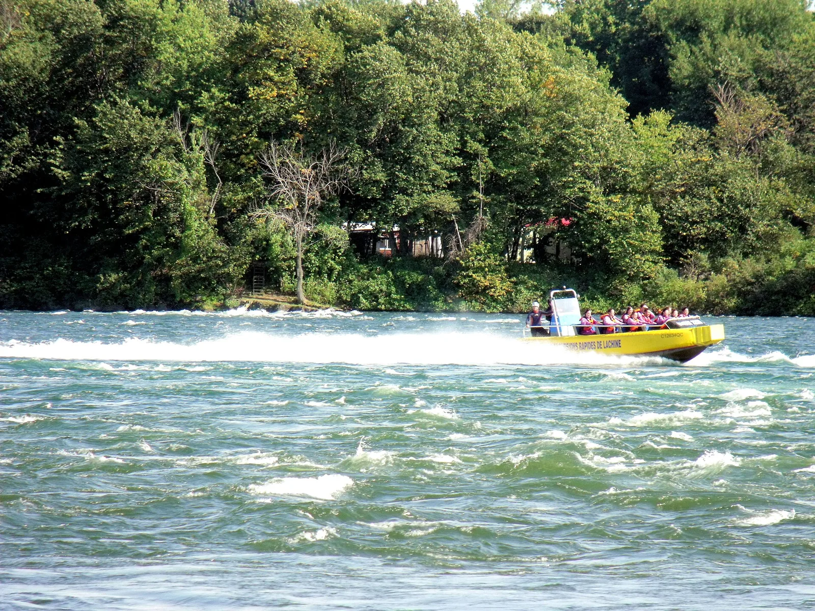 A yellow jet boat full of passengers crashing through the white water of the Lachine Rapids