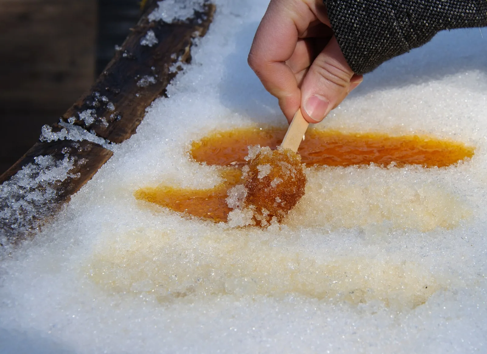 Hot maple syrup being rolled onto a wooden stick on a tray of snow to make maple taffy