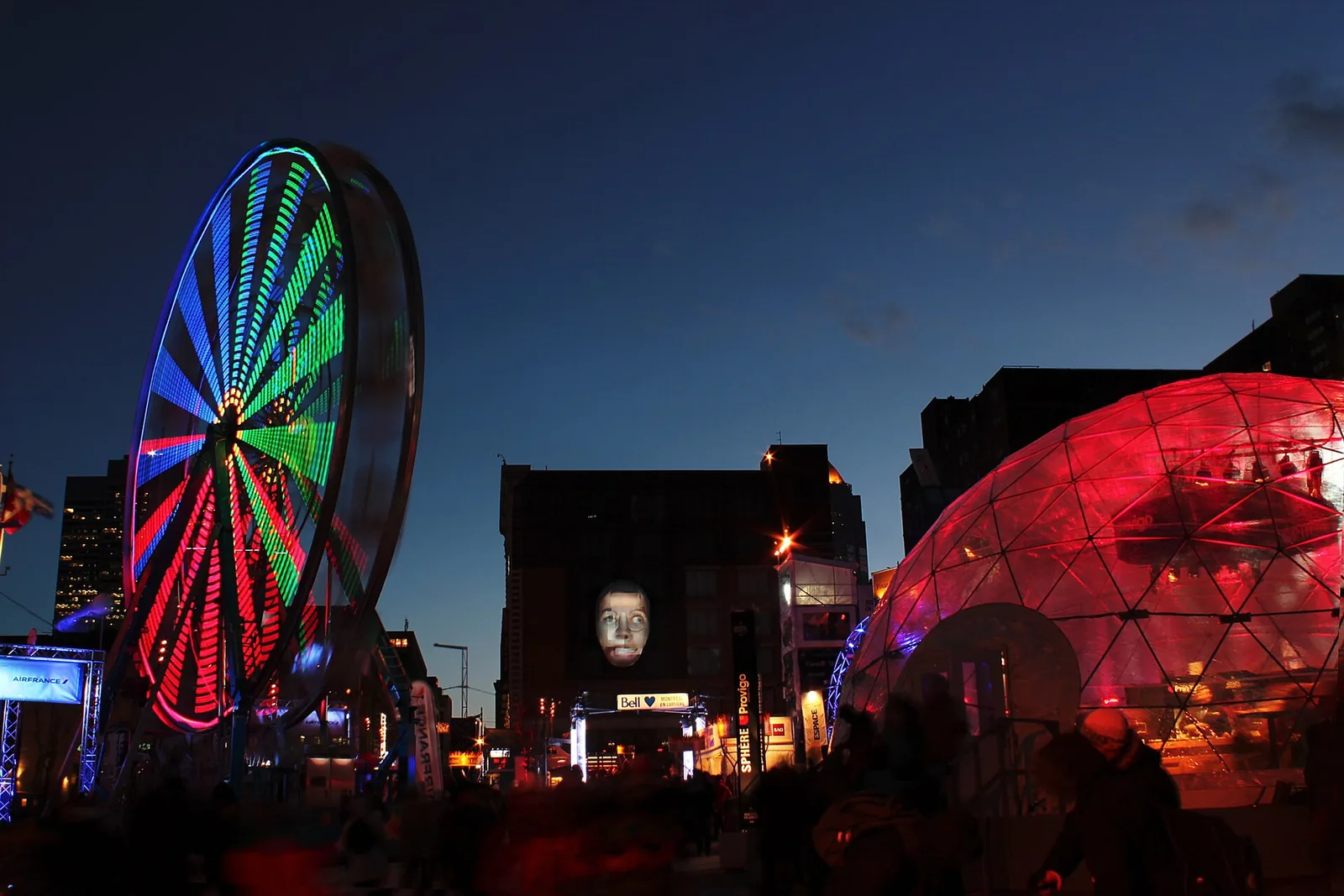 Illuminated Ferris wheel and glowing red dome at the Montréal en Lumière outdoor site in the Quartier des spectacles