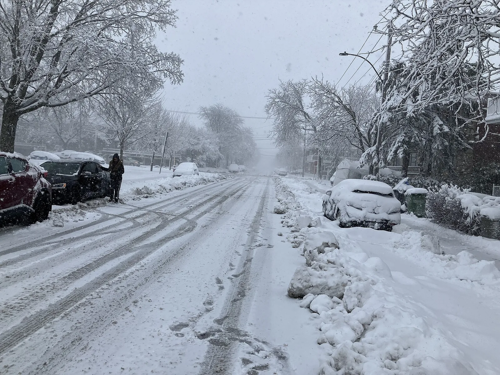 Snow-covered residential street and buried parked cars during a Montreal snowstorm, ideal weather for a Nordic spa Montreal afternoon