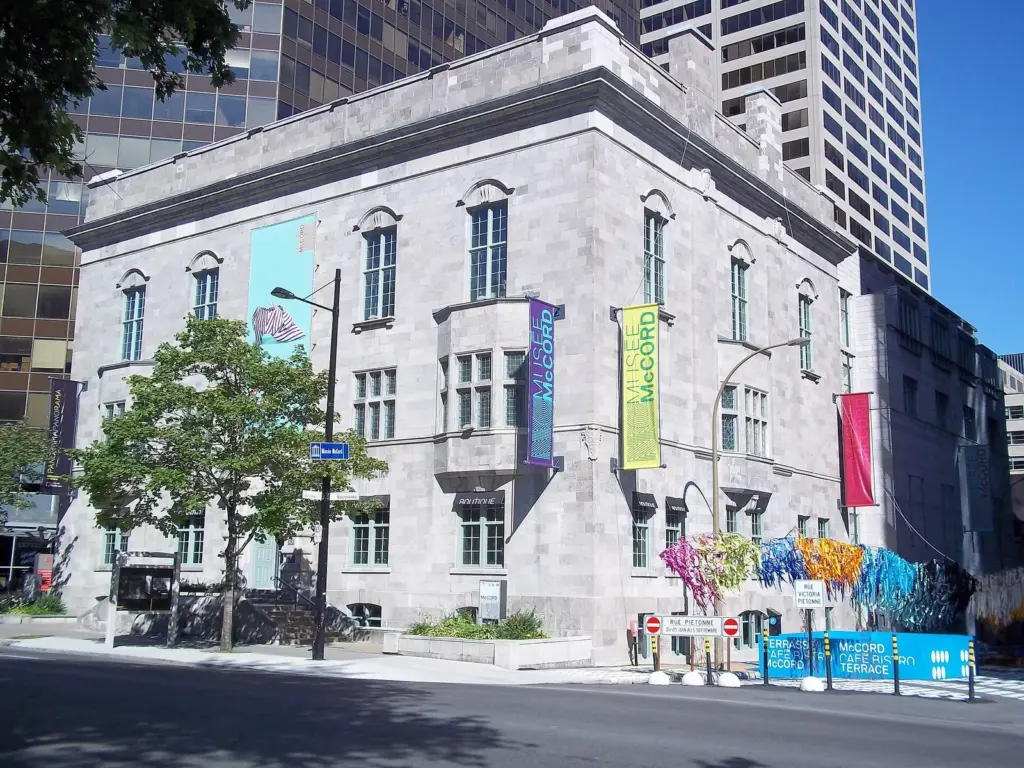 The grey stone McCord Stewart Museum on rue Sherbrooke with banners and downtown towers behind