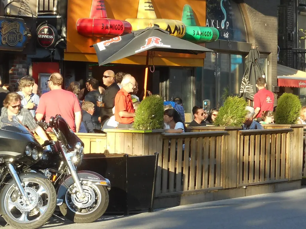 People eating and drinking on a busy wooden terrasse on rue Saint-Denis in Montreal on a summer evening