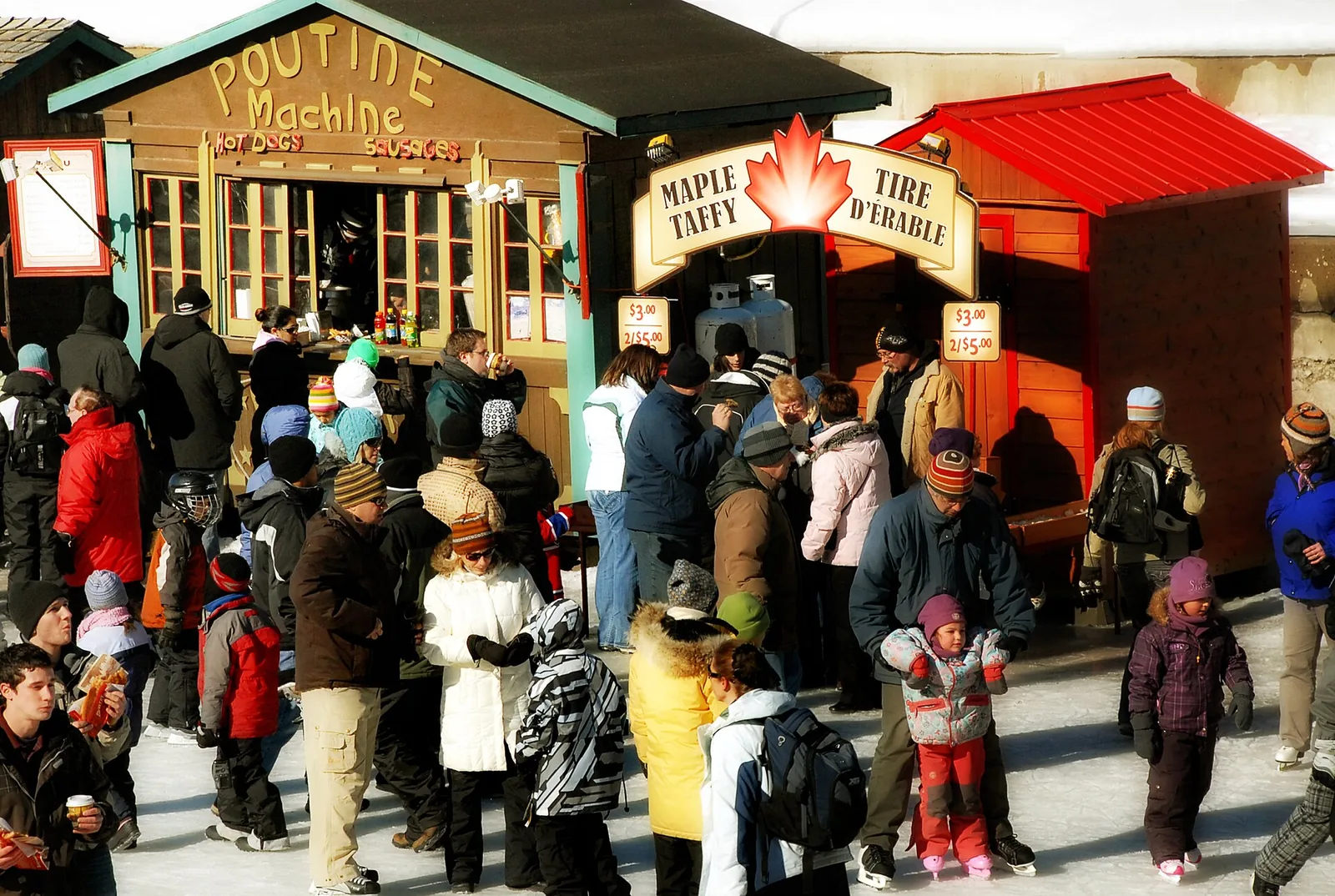 Crowd in snowsuits queuing at wooden chalets selling poutine and maple taffy at a winter festival