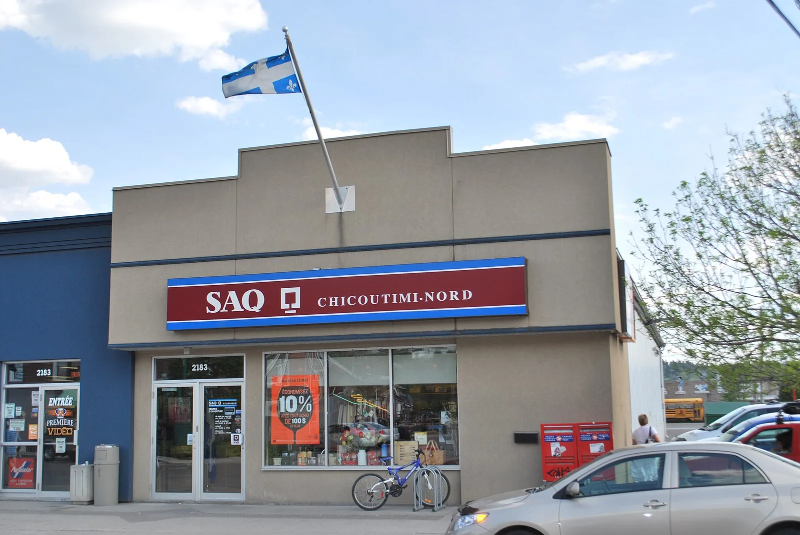 An SAQ liquor store branch with its red and blue sign and a Quebec flag