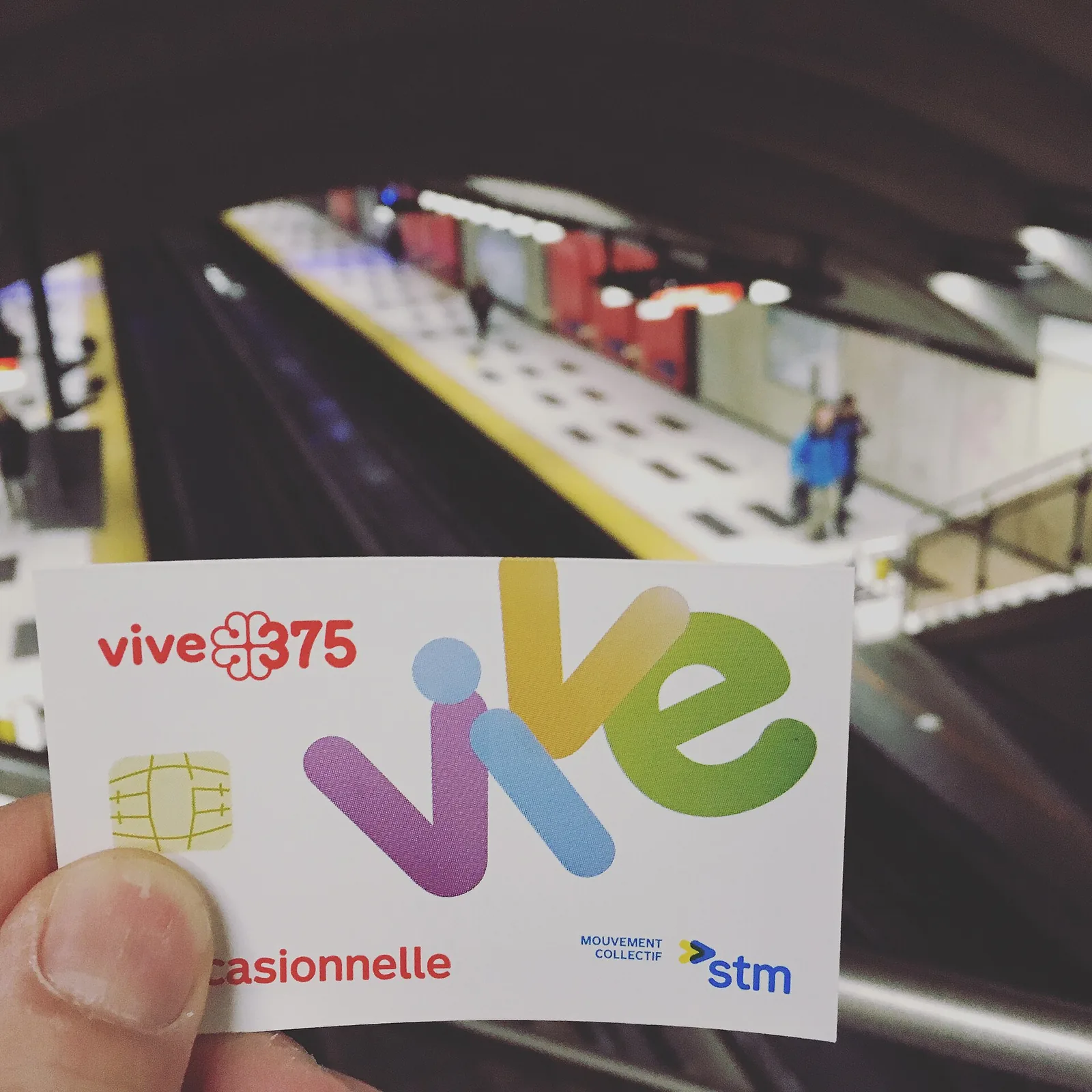 A hand holding an STM transit fare card on a Montreal metro platform