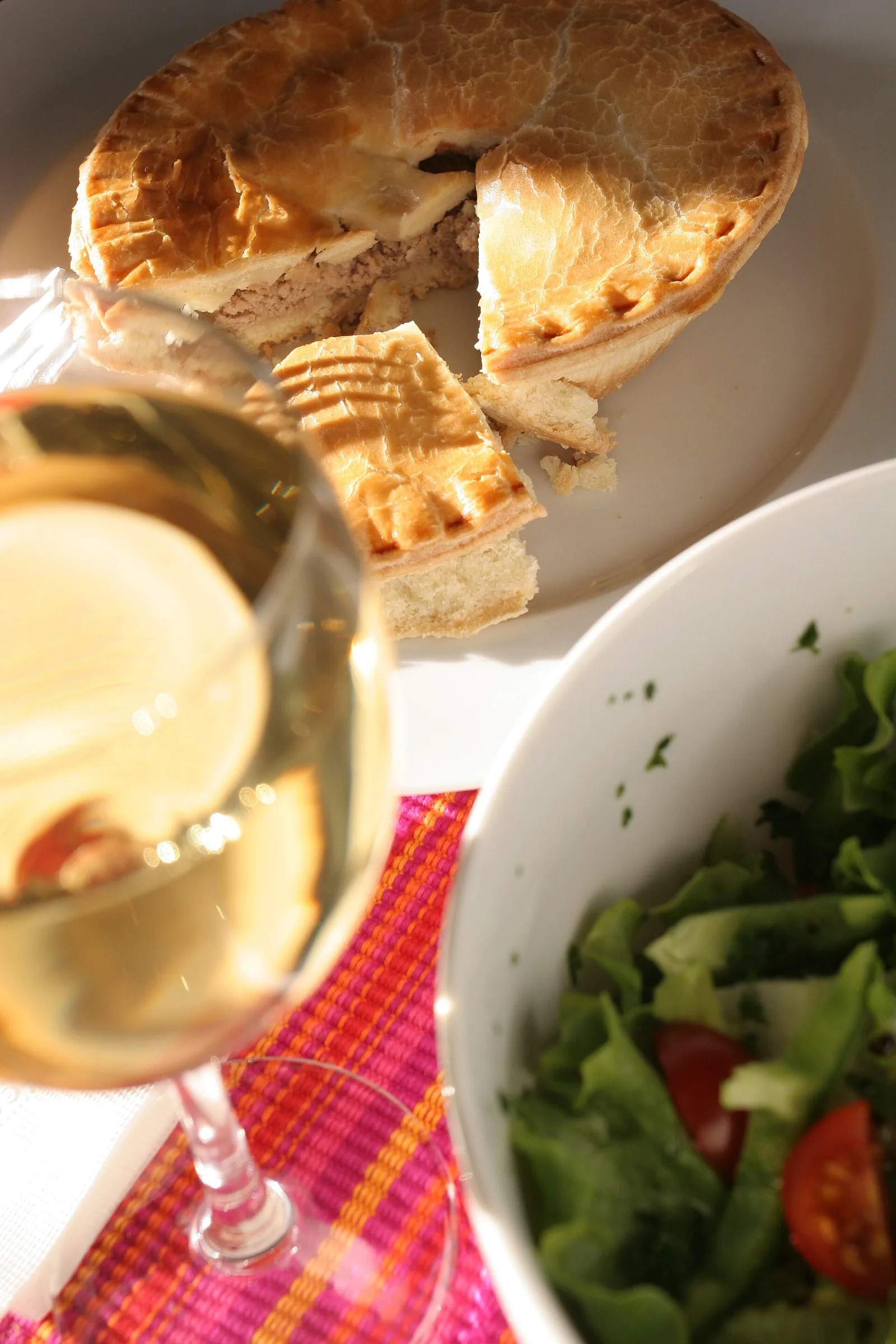 A tourtière, the spiced Quebec meat pie, sliced on a table with salad and a glass of white wine