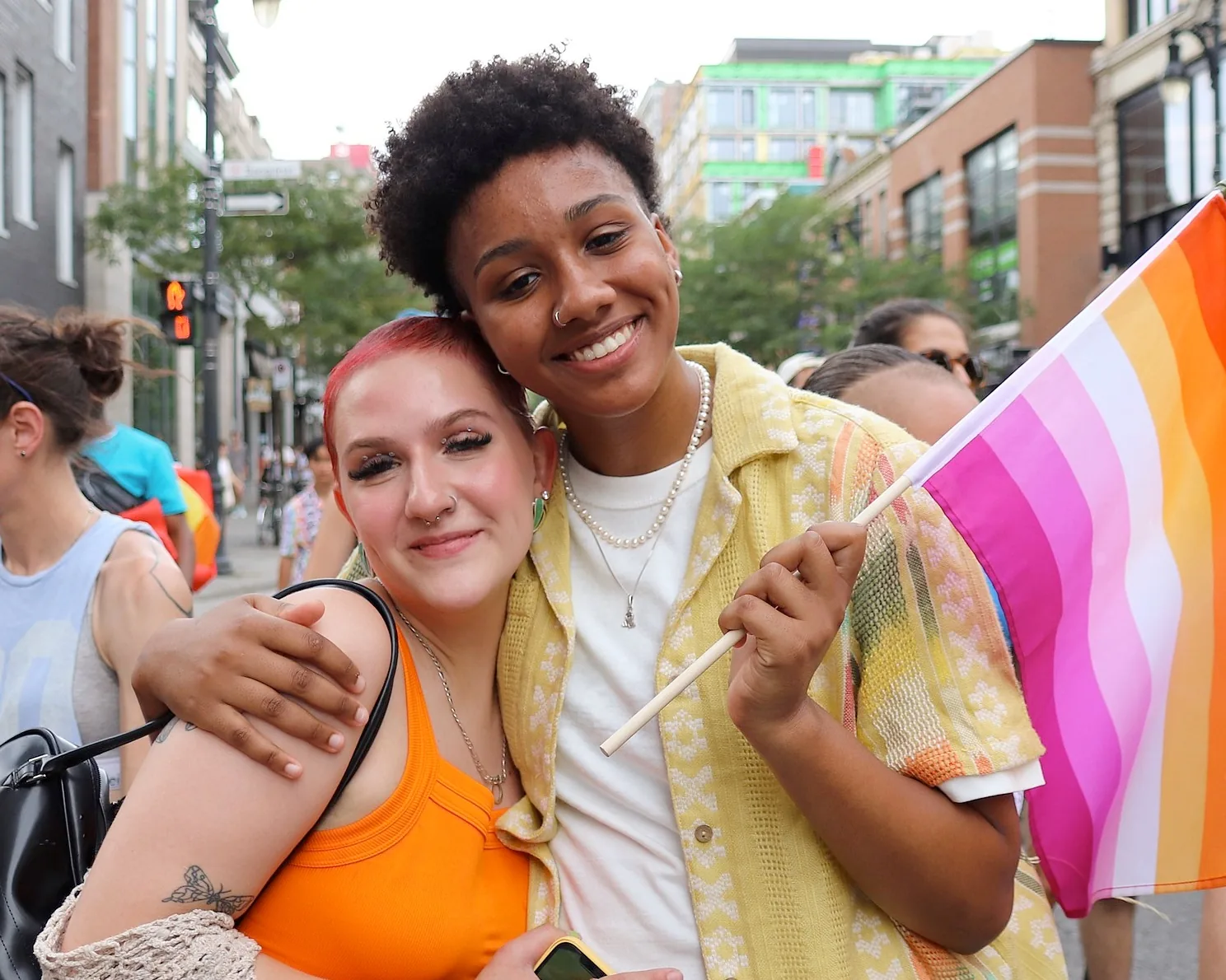 Two smiling marchers with a Pride flag at the Montreal Pride march on a summer street